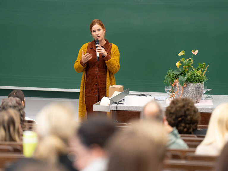 Eine Frau spricht vor einer Tafel stehend zum Publikum.