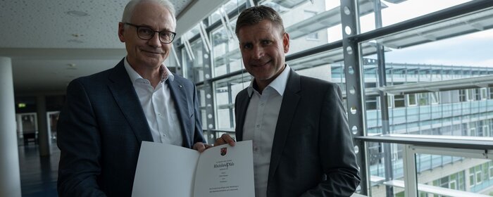Zwei Männer stehen zusammen und halten eine Urkunde.