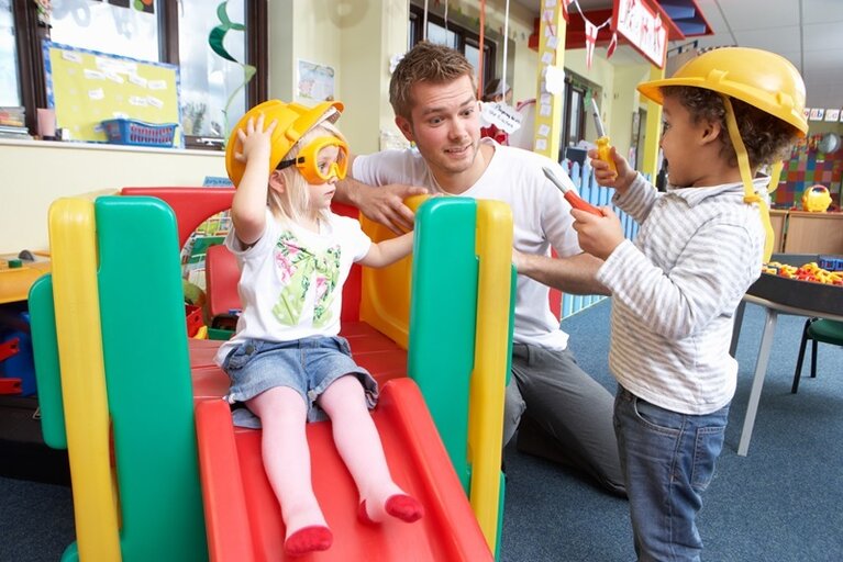 Ein Erzieher spielend mit zwei Kindern in der Kita.