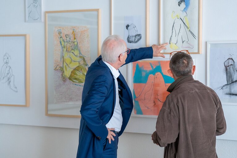 Zwei Männer stehen vor Kunstobjekten, die an einer Wand hängen