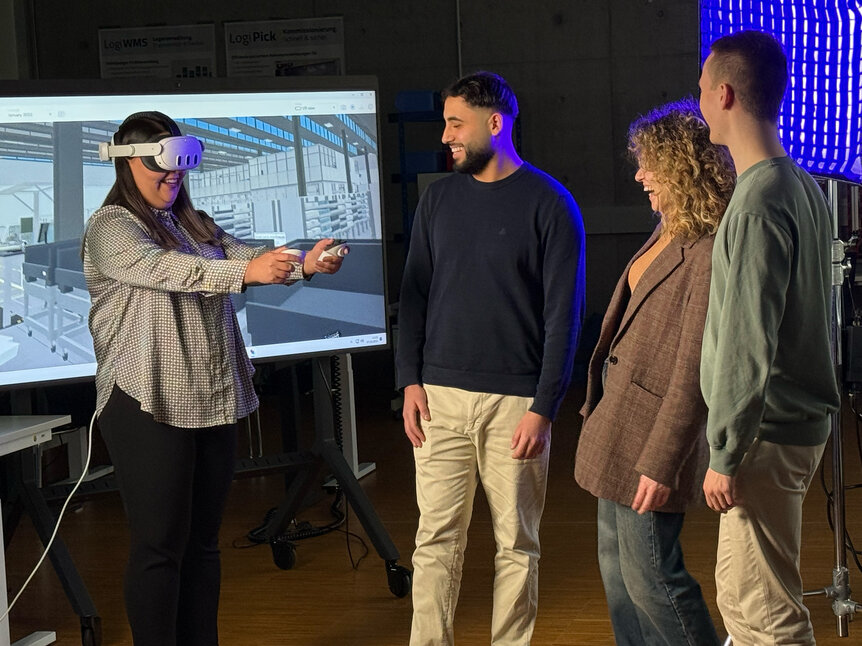Studierende mit VR-Brille vor einem großen Monitor