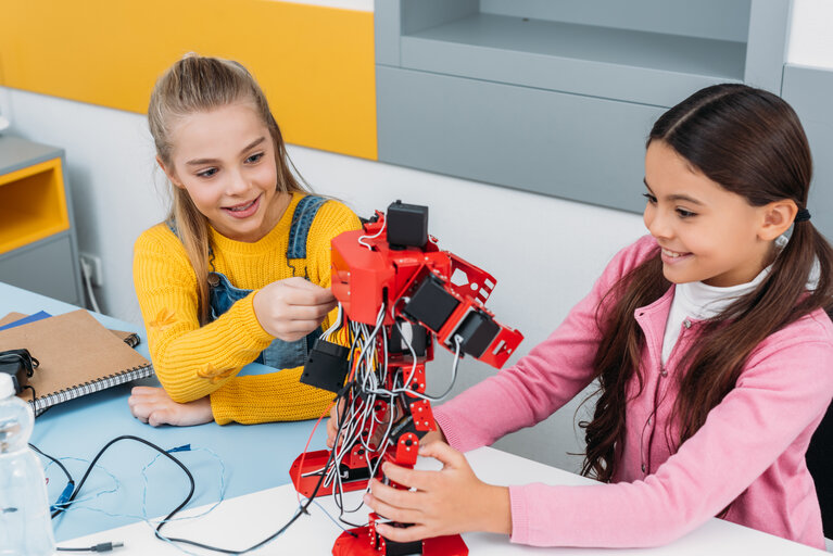 Zwei Mädchen experimentieren mit einem Roboter