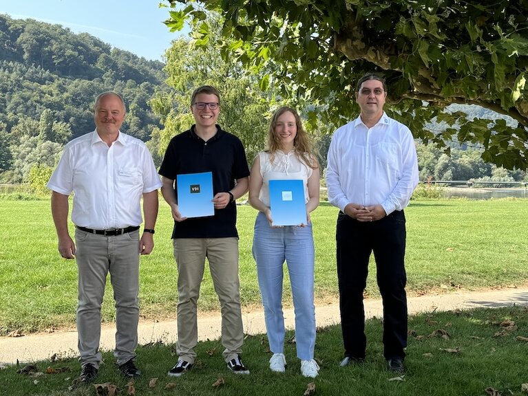 Eine Gruppe von vier Personen steht auf einer Wiese. Die Preisträgerin und der Preisträger halten ihre Urkunde in der Hand. 