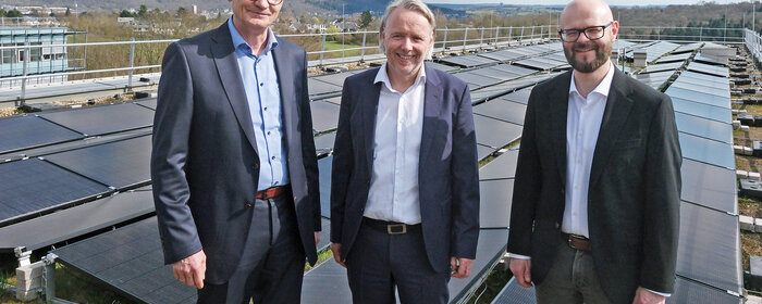 Drei Männer stehen neben einer Photovoltaik-Anlage auf dem Dach der Hochschule Koblenz