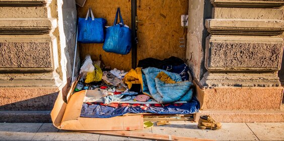 Das Lager eines Obdachlosen im Hauseingang mit Decken und Taschen.