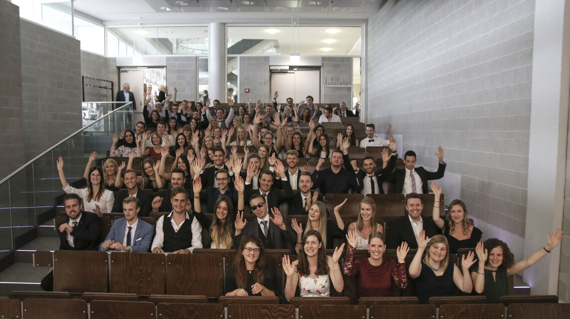 Absolventinnen und Absolventen mit gehobenen Händen im Hörsaal