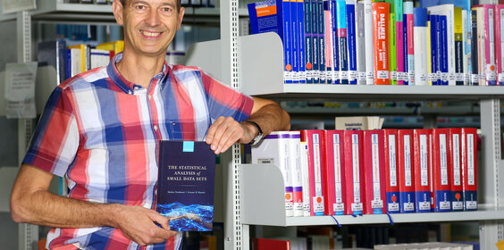 Professor Neuhäuser mit seinem Buch in der Bibliothek der Hochschule.